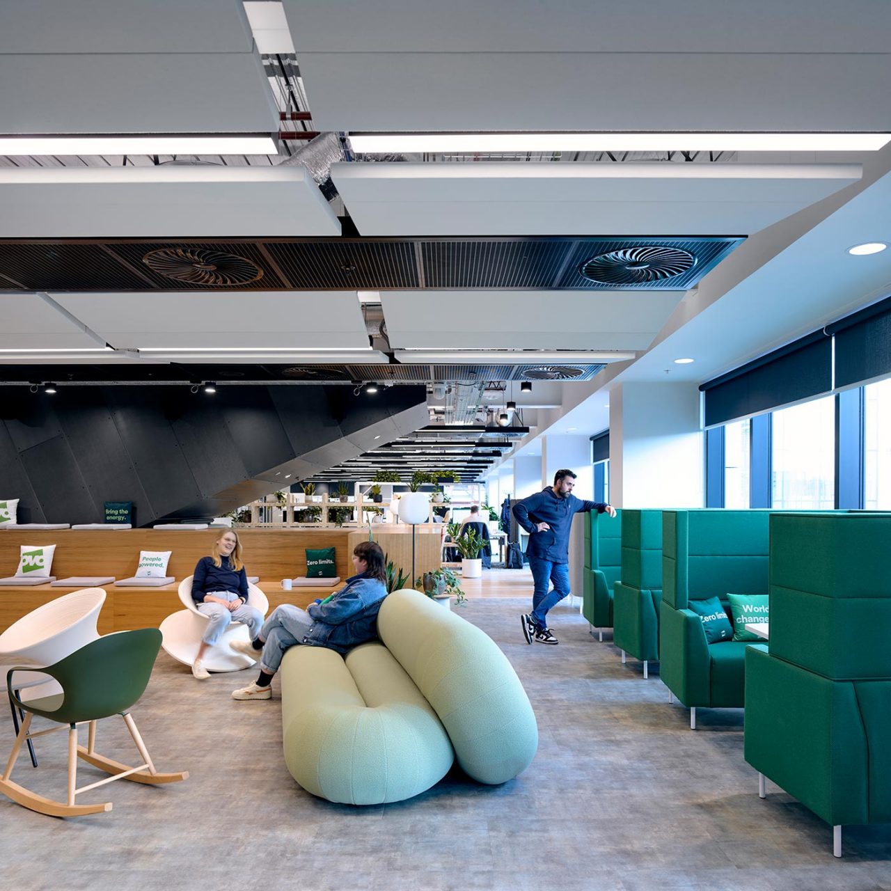 Green loop sofa in the foreground and a variety of furniture and office pods with people lounging or standing in the spaces