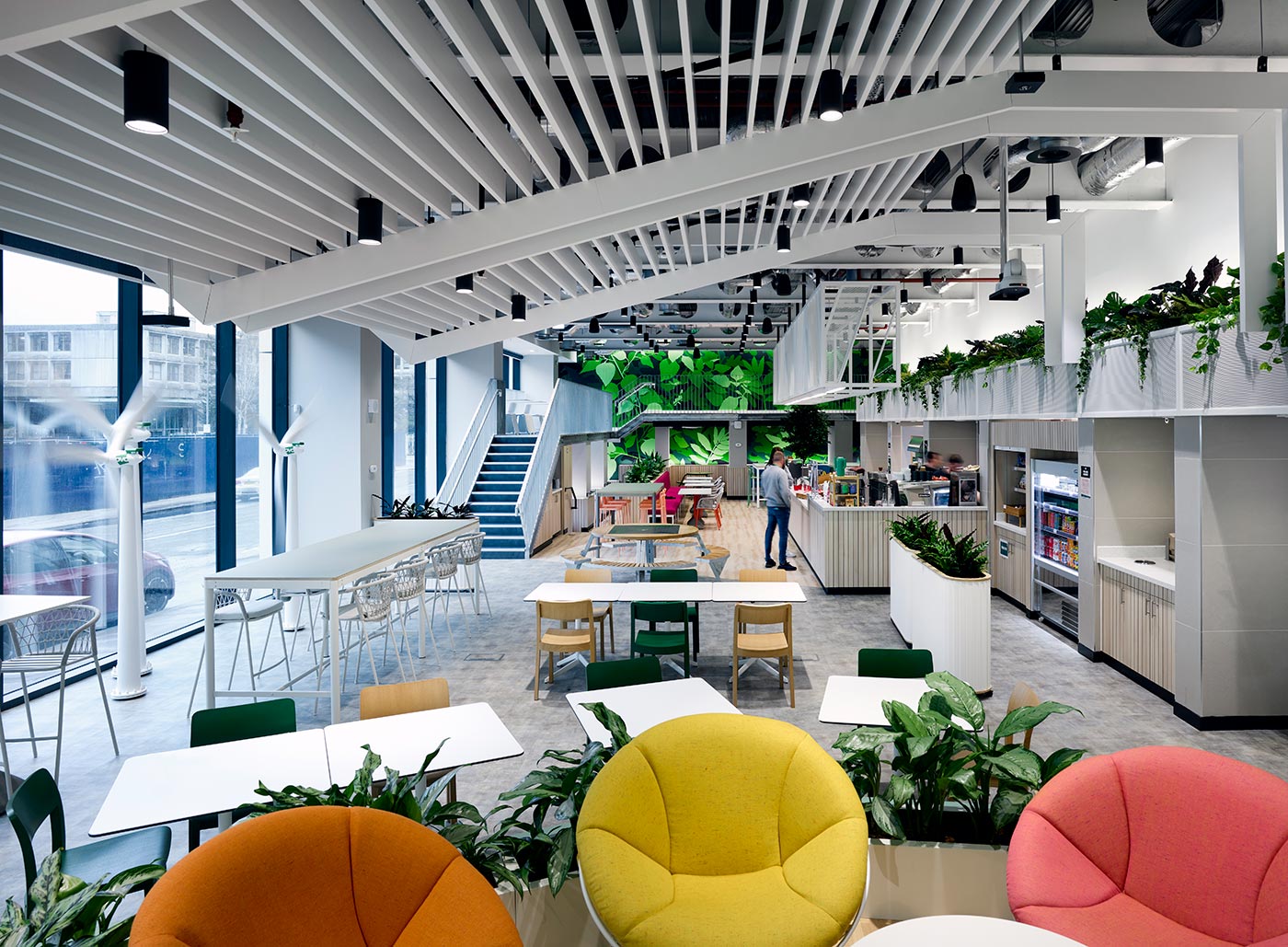 Soft seating in the foreground of an office cafe space with green leaf mural on the back wall