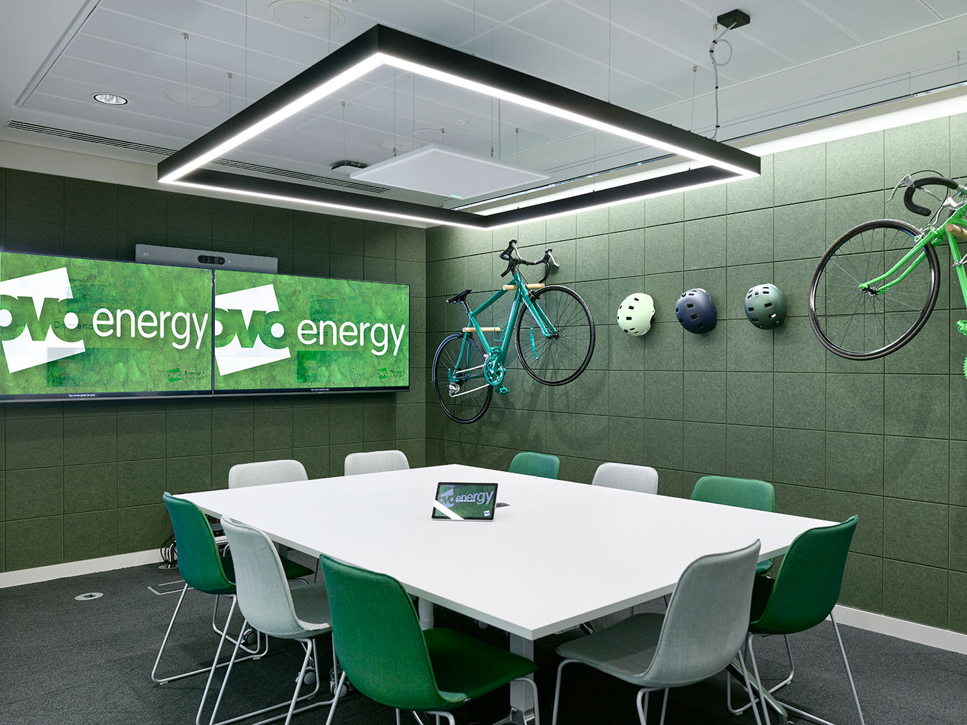 Meeting room with green walls and a table and chairs in foreground. The brand name OVO energy is on a board on the wall and bicycles are hanging on one wall as a display
