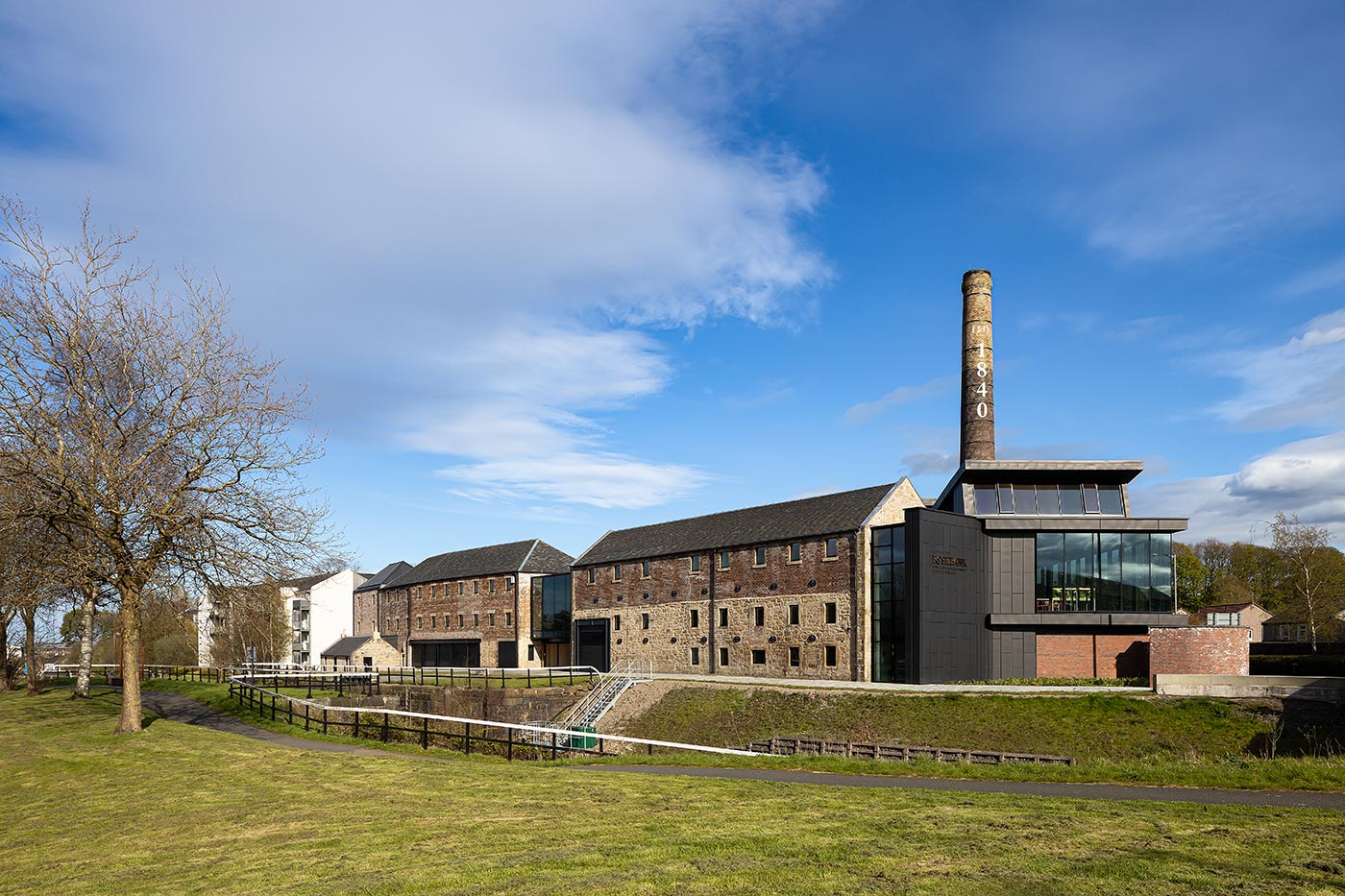 Rosebank Distillery pictured alongside the canal with grass in the foreground