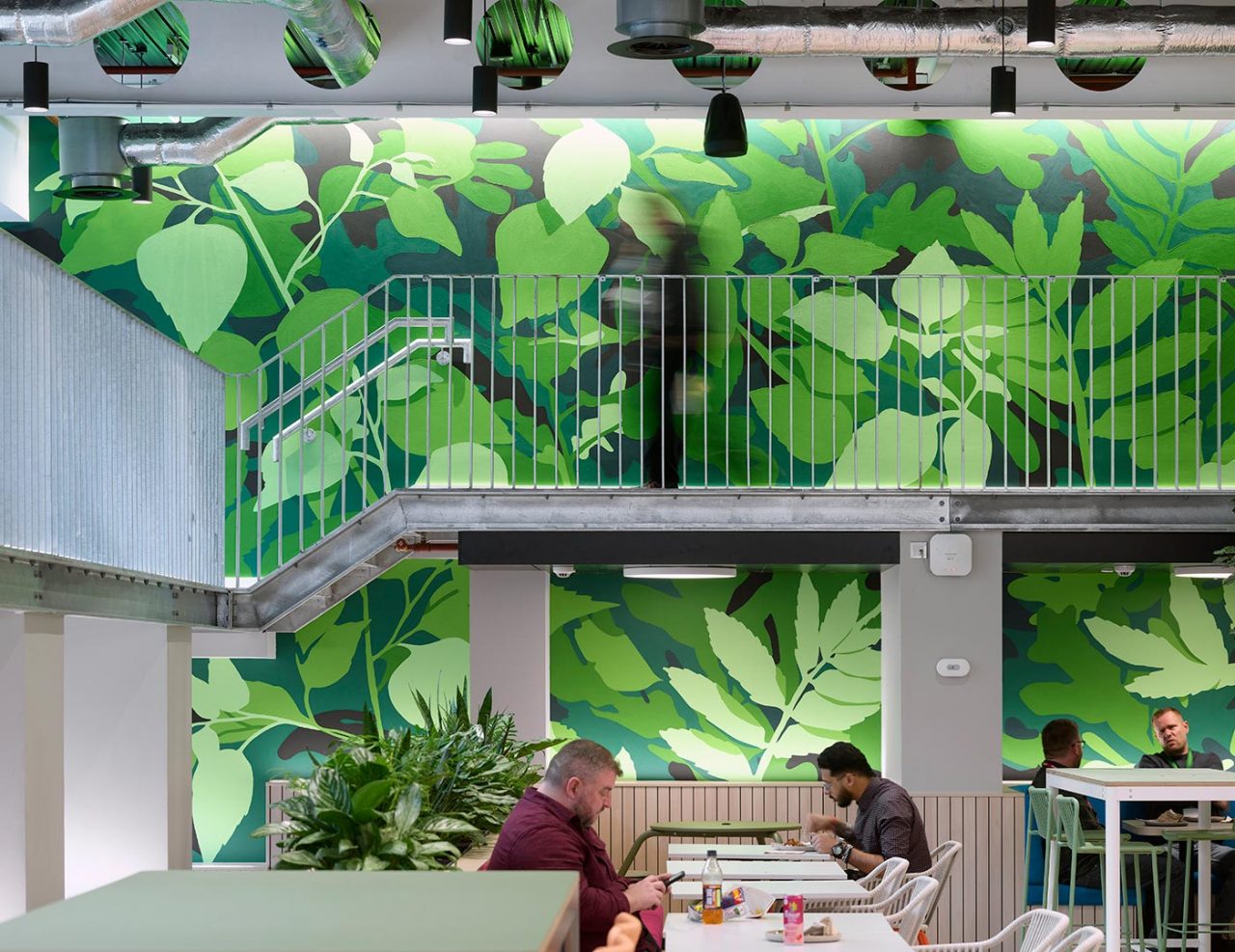 Men seated at cafe table with large green botanical mural on the wall behind